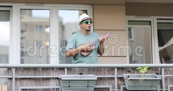 一个戴着胡子的帽子的人在阳台上的四弦琴上玩耍视频的预览图