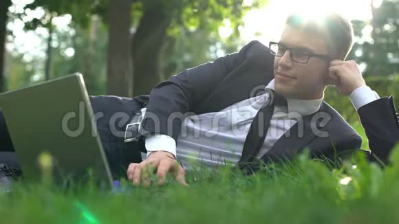 商人躺在公园的草地上手提电脑与大自然和谐相处视频的预览图