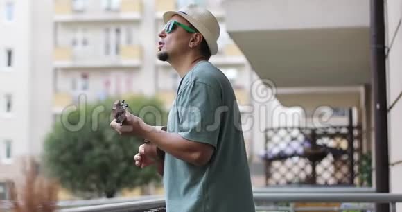 夏天一个戴着胡须的帽子的人在阳台上玩四弦琴视频的预览图