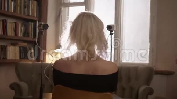 穿着黑色的金发女人光着肩膀坐在复古电视前视频的预览图