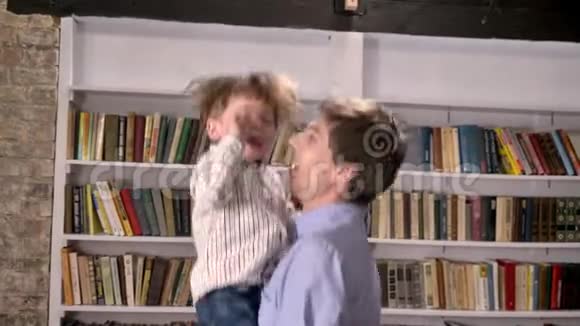 年轻的父亲抱着他的小儿子在图书馆里跳跃微笑而快乐视频的预览图