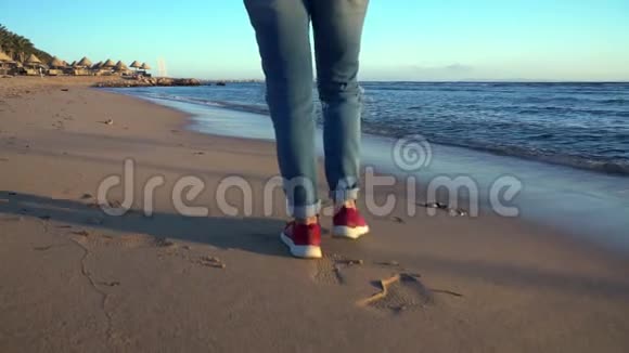 穿牛仔裤和运动鞋的人在海滩上散步视频的预览图