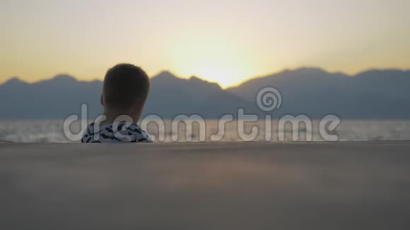 穿衬衫的男孩蝙蝠坐在海边视频的预览图