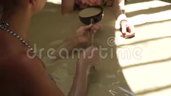 美丽的女人在水疗中心的泥浴中放松年轻女子沐浴在泥浆温泉里用勺子把身体倒在水里视频的预览图