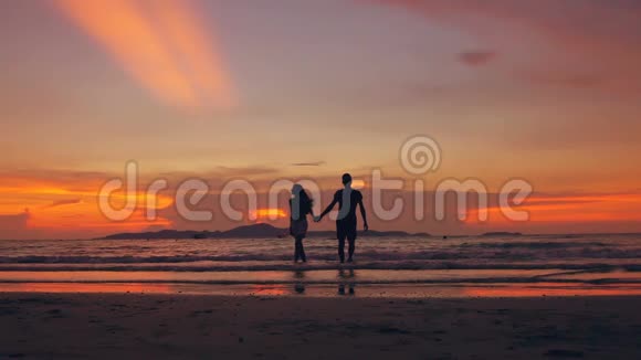 在海边的夕阳下一对幸福的情侣在海滩上漫步视频的预览图