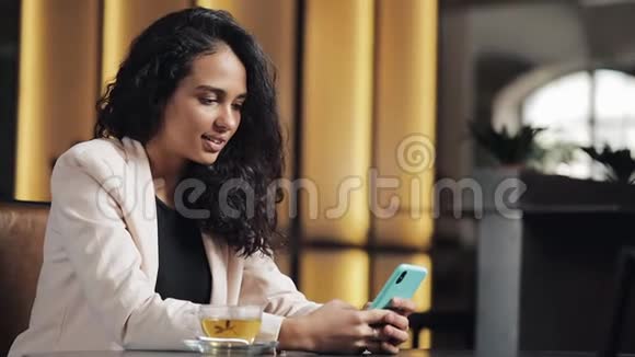 年轻的商务女性在咖啡馆喝茶并使用手机进行社交网络和电子邮件晚餐和网络视频的预览图