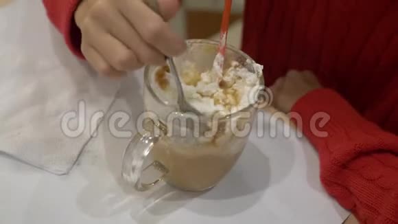 一个棕色头发的女孩在咖啡馆里喝着带棉花糖和鲜奶油的热巧克力享受着长发饮料视频的预览图