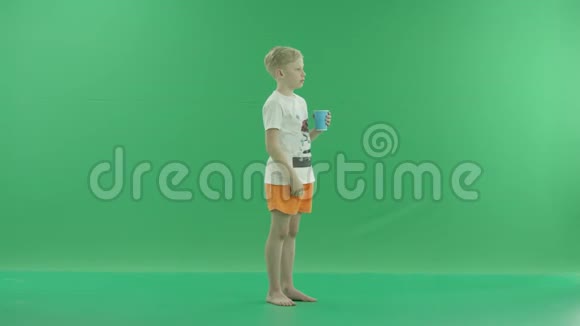 一个年轻的金发男孩喝水是为了在炎热的日子里提神他侧着身子站在绿色屏幕上视频的预览图