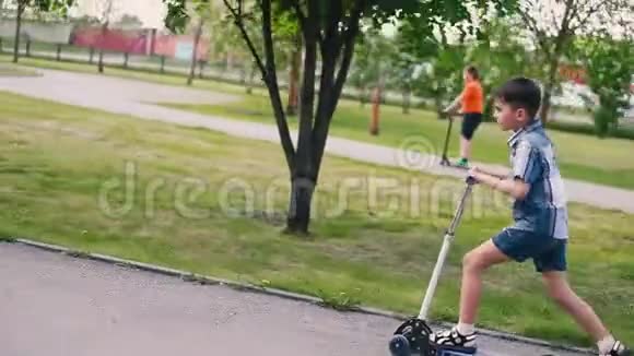 这个男孩在夏天阳光明媚的天气里在公园里骑滑板车心情很好高清高清视频的预览图