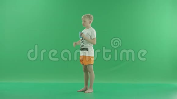 一个年轻的金发男孩喝水是为了在炎热的日子里提神他侧着身子站在绿色屏幕上视频的预览图