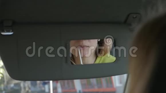 年轻的金发女人在车里画着她的嘴唇看着后视镜慢动作视频的预览图