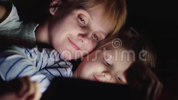 快乐的母亲和她的女儿我一起玩平板电脑面对面躺在床上视频的预览图