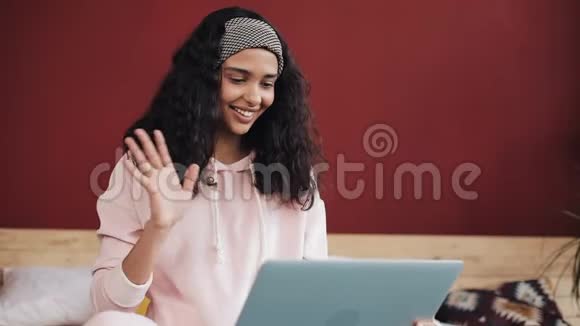年轻漂亮的女人坐在床上高兴地和一个人聊天在她的笔记本电脑上的视频电话慢动作视频的预览图