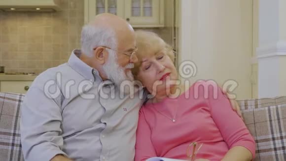 可爱的老夫妇坐在家里的沙发上拥抱视频的预览图