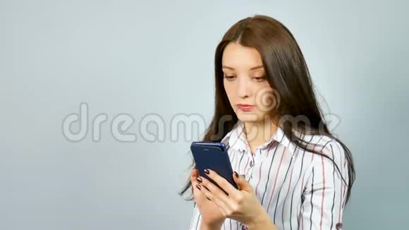 戴着深色长发的严肃女商人在手机上聊天穿衬衫的年轻女子谈蓝色智能手机视频的预览图
