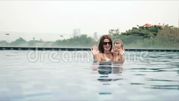 美丽的母亲和她的儿子站在游泳池里在温暖的夏日度假时大笑的肖像视频的预览图