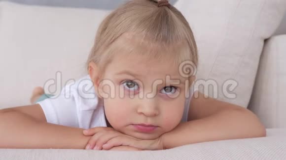 一个小女孩躺在柔软的沙发上看着电视屏幕视频的预览图