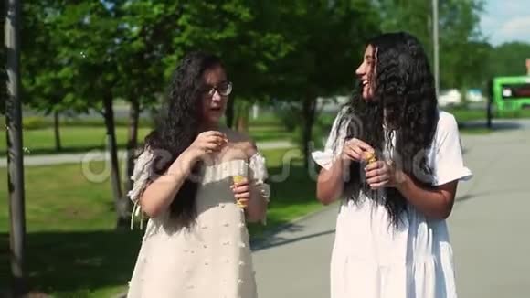 两个心情愉快的朋友在公园散步在夏天晴朗的天气做肥皂泡视频的预览图