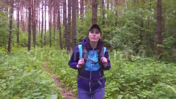 一个女孩带着旅游背包穿过树林的肖像视频的预览图