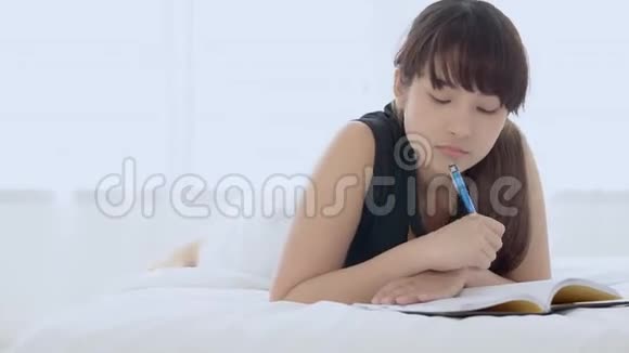 美丽的肖像年轻的亚洲妇女放松躺在床上思考想法和写书或日记在卧室在家里视频的预览图
