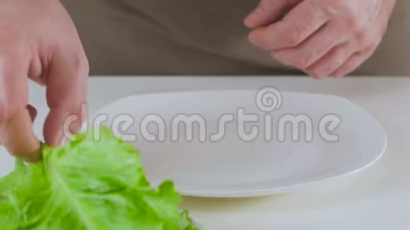 一个人在做素食午餐的时候把绿生菜叶铺在白色盘子上视频的预览图
