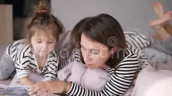 年轻的母亲正在为躺在床上的可爱的小女儿读一个故事小男孩正在翻阅这本书视频的预览图
