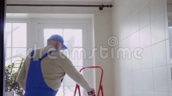 穿蓝色防护衣的老人在窗户上修檐口视频的预览图