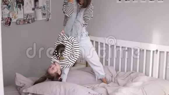棕色头发的母亲和女儿在床上玩得很开心把她颠倒过来摇摆慢动作视频的预览图