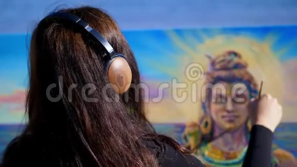 夏天河边海滩上日出时一位戴着棕色大耳机的美女艺术家手里拿着画笔视频的预览图