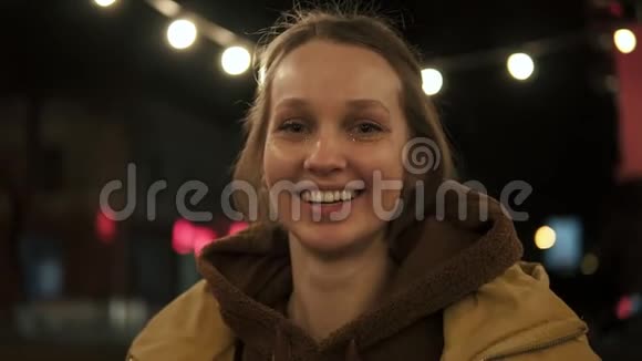 前镜头的年轻女孩在夜街微笑和嬉戏伸出舌头后面的街灯视频的预览图