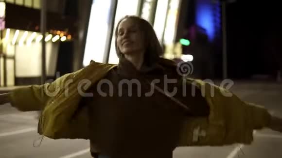 可爱开朗的女孩在夜晚的一个明亮的停车处转来转去在外面手工射击视频的预览图