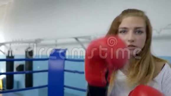 拳击场上的女运动员戴着拳击手套准确地挥拳并在训练时看着摄像机视频的预览图
