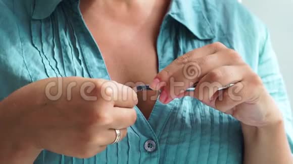 年轻女子在家做指甲女人用指甲镊子切割角质层家庭指甲和防雹护理视频的预览图