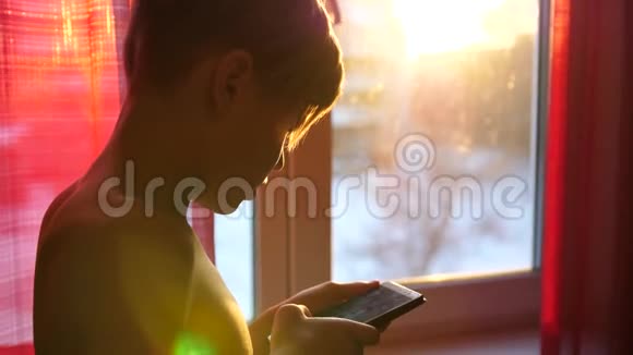 一个年轻人站在窗户附近手里拿着一部日落的时候太阳光线穿过房间视频的预览图