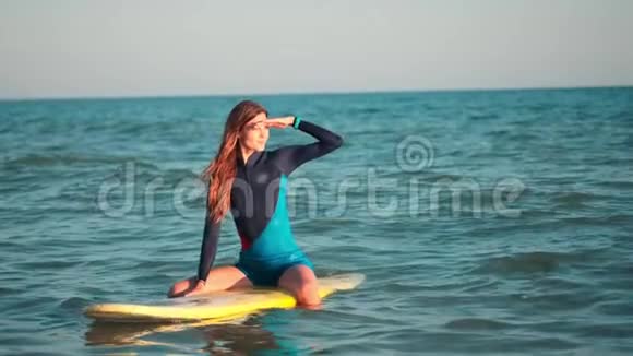 慢动作年轻苗条的冲浪女孩看日落漂浮在开阔的海面上等待海浪和视频的预览图