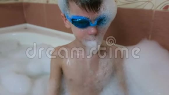 男孩67年在泡沫和护目镜游泳坐在浴室面的特写视频的预览图