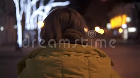 美丽温柔的女孩穿着外套穿过夜城转身微笑着跟踪射击视频的预览图