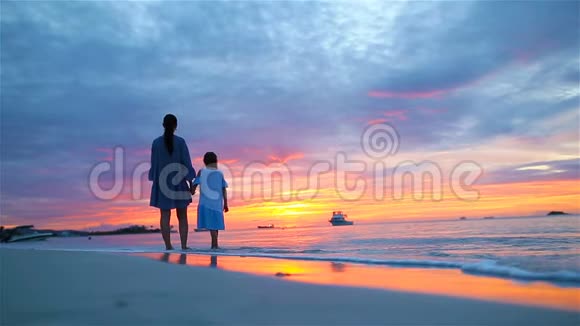 小女孩和快乐的妈妈剪影在美丽的日落海滩上地平线上惊人的色彩视频的预览图