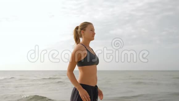 年轻女子在海滩上放松和日光浴美丽的女人在做瑜伽站在沙滩上摆出海景视频的预览图