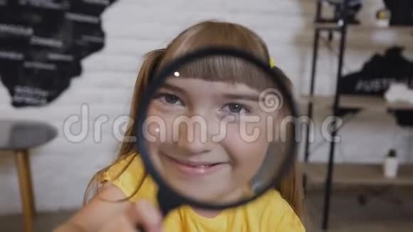 一个在放大镜里玩耍的可爱女孩的肖像可爱的小女孩透过放大镜和视频的预览图