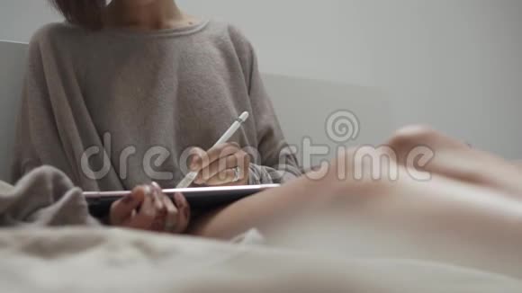 女人在卧室里用手写笔和平板电脑浏览网站视频的预览图