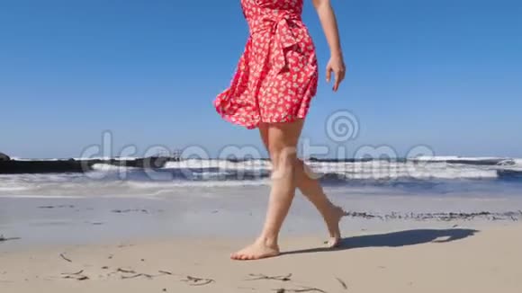 年轻女子的腿在沙滩上行走海浪很大穿着红色裙子的年轻女子在塞浦路斯海滩漫步视频的预览图