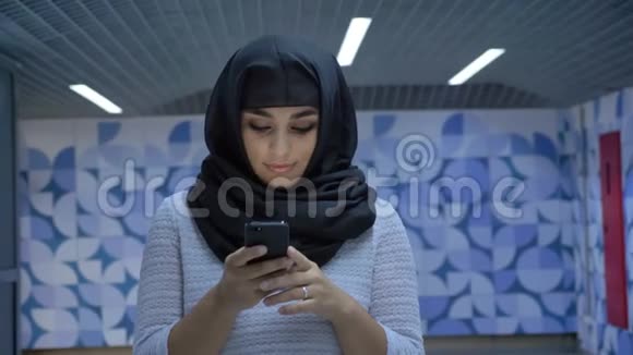 年轻迷人的穆斯林妇女戴着头巾在地下通道的智能手机上输入信息在镜头下观看宗教概念视频的预览图