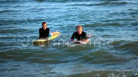 两个冲浪者在公海的冲浪板上游泳等待海浪视频的预览图