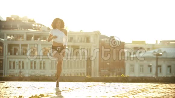 一位穿着小短裤的年轻女子在屋顶上表演迷人的性感舞蹈灿烂的日落视频的预览图