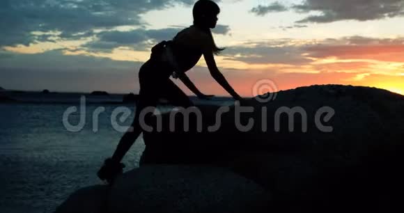 黄昏时分女人站在沙滩上的岩石上视频的预览图