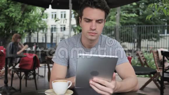 男人一边喝咖啡一边浏览平板电脑一边坐在咖啡厅露台上视频的预览图
