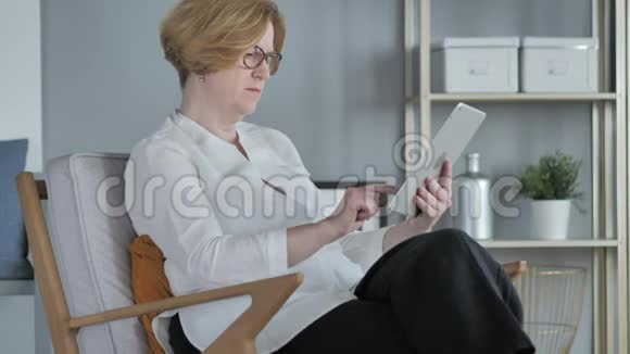 老年妇女在平板电脑上浏览互联网坐在沙发上视频的预览图
