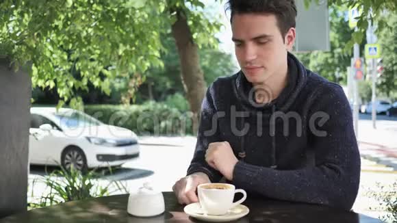 年轻人把糖和咖啡混合在一起坐在咖啡馆的露台上视频的预览图