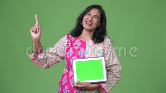 成熟快乐美丽的印度女人在思考时展示数字平板电脑和手指视频的预览图